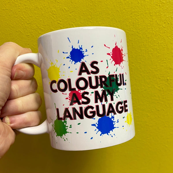 As Colourful as my Language White Mug with red, blue, green and yellow splashes, against a yellow background.